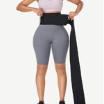 Femme enroulant une longue bande amincissante noire en latex autour de sa taille, vue de face.