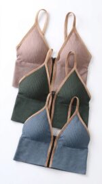 Trois bralettes côtelés à zip devant en rose poudré, vert forêt et bleu ardoise avec passepoil beige, à plat.