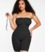 Femme en body galbant noir sans bretelles tenant une bretelle, vue de face.
